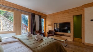 Ein Schlafzimmer mit einem Bett, einer Bank, einem Fernseher und einer Steinsäule vor dem Fenster.