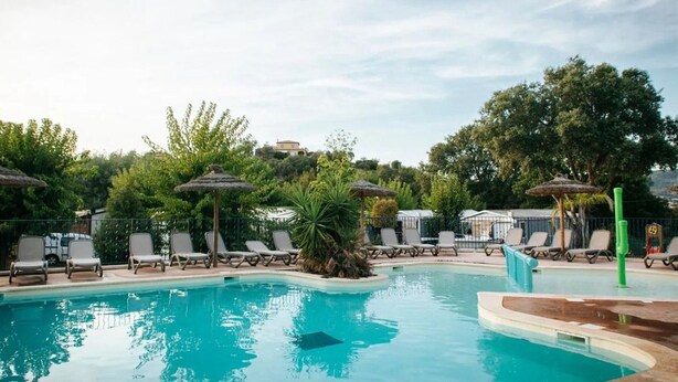 A swimming pool with lounge chairs and umbrellas, surrounded by greenery and trees. - Chalet in Bormes-les-Mimosas with terrace (Bormes-les-Mimosas)