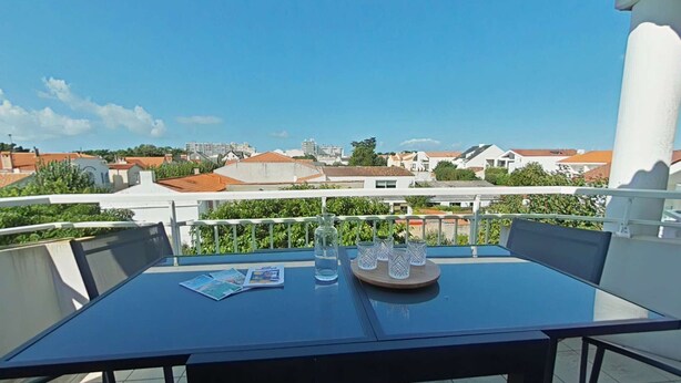 A balcony with a table, chairs, a glass pitcher, and glasses.