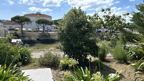 A courtyard with a pond, surrounded by greenery and a white building with a red roof.