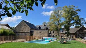 Une maison en pierre avec une piscine, entourée d’une clôture en bois et d’une pelouse verdoyante.
