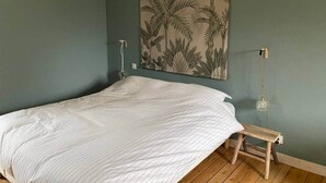 Une chambre avec un grand lit, un banc en bois, un luminaire suspendu et une tapisserie murale.