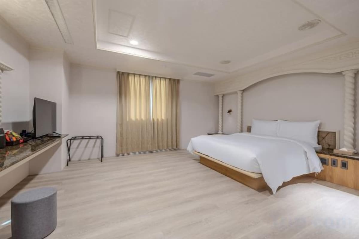 A hotel room with a bed, a desk with a computer, a television, and a window with curtains.