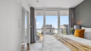 A bedroom with a large bed, a view through a sliding glass door to a balcony, and a modern interior design.