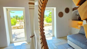 Un interior moderno con una escalera de caracol, un sofá y vistas a palmeras a través de una puerta.