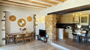 Amplia sala de estar con chimenea de piedra, vigas de madera en el techo y una cocina con gabinetes blancos y encimera negra.