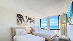 A hotel room with two beds, a view of the ocean, and artwork on the walls.
