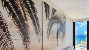 A room with a large beach-themed wall mural, a bed with white bedding, and a view of the ocean through a large window.
