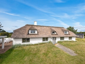 A thatched-roof house with a small porch and a pathway leading to the entrance.