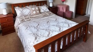 A bedroom with a wooden bed, two bedside tables, a nightstand, a round table with a pink tablecloth, and two framed pictures on the wall. - Master retreat at Private Estate Near Perth CBD (Stirling)