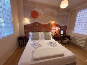 Een hotelkamer met een bed, twee nachtkastjes, een bureau, een stoel, een radiator en een muurschildering.