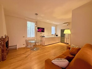 A modern living room with a glass dining table, a sofa, and a kitchen in the background.