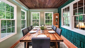 Comedor con una mesa de madera dispuesta para seis personas, rodeada de sillas, un centro de mesa con planta y una estantería al fondo.
