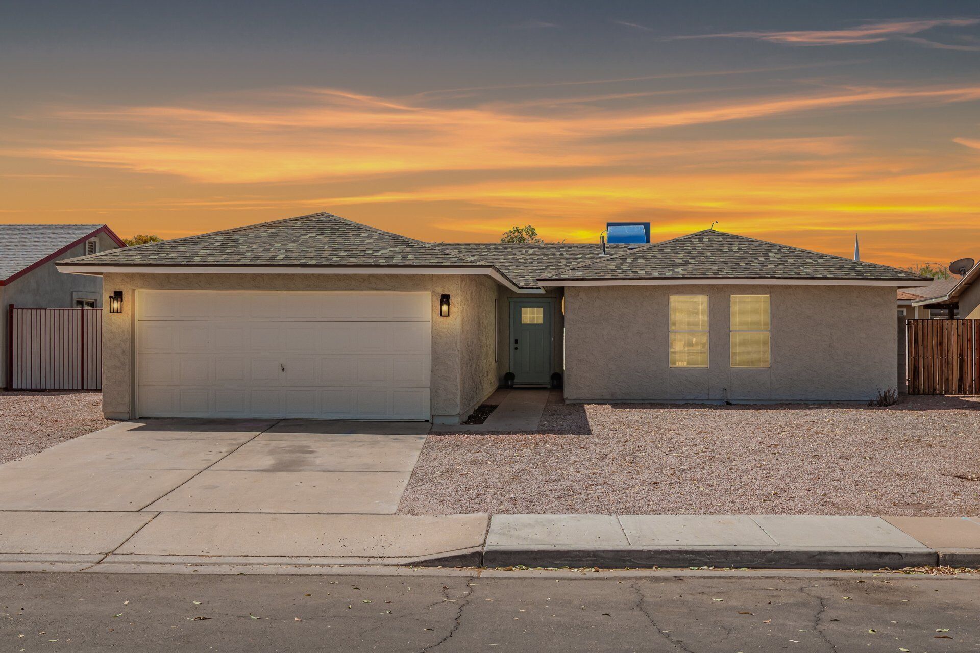 A two-car garage house with a small attached shed, a driveway, and a gravel yard.