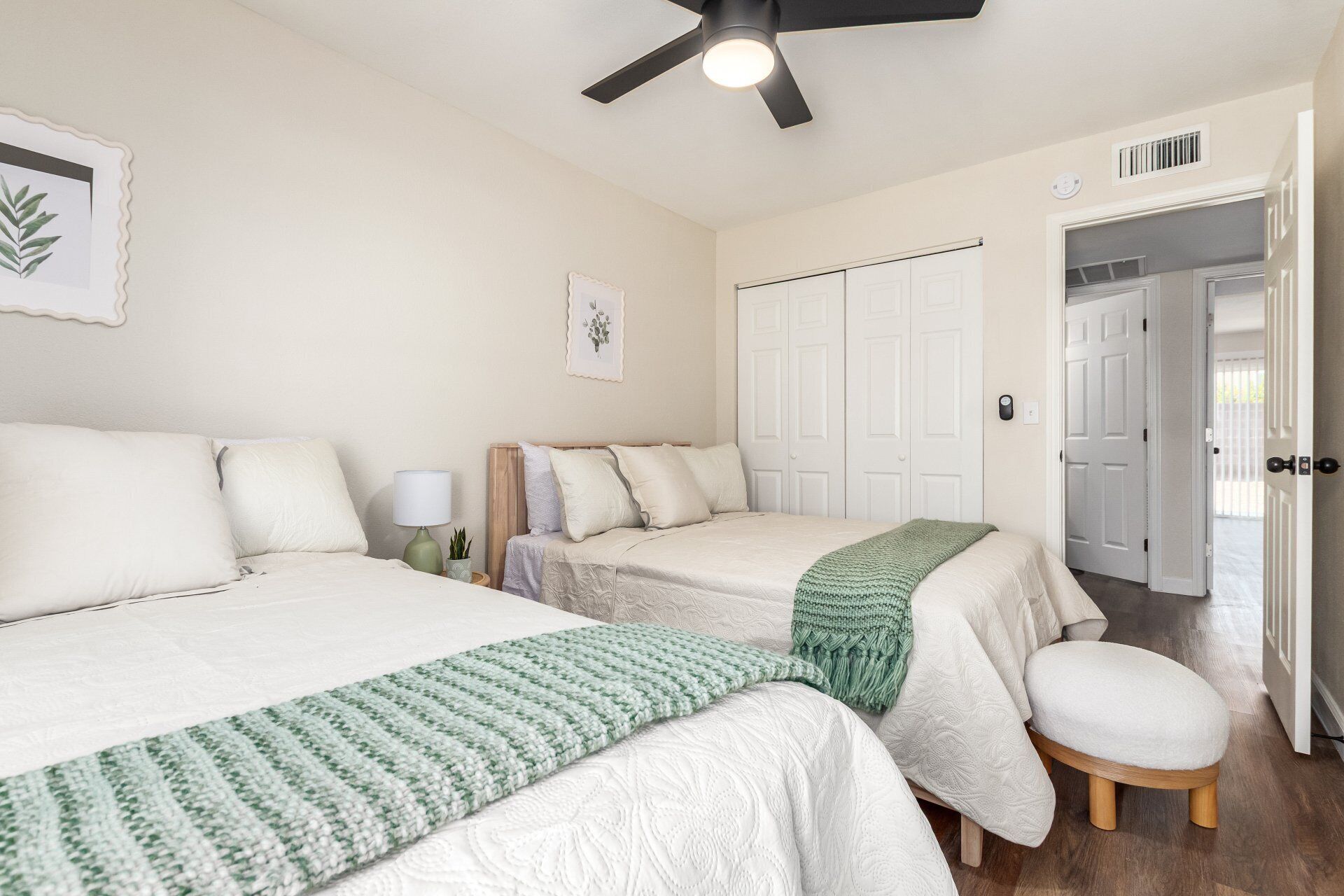 Une chambre avec deux lits, un ventilateur de plafond, une porte et un petit tabouret.