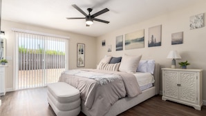 A bedroom with a bed, a nightstand, a ceiling fan, and a sliding glass door leading to a patio.