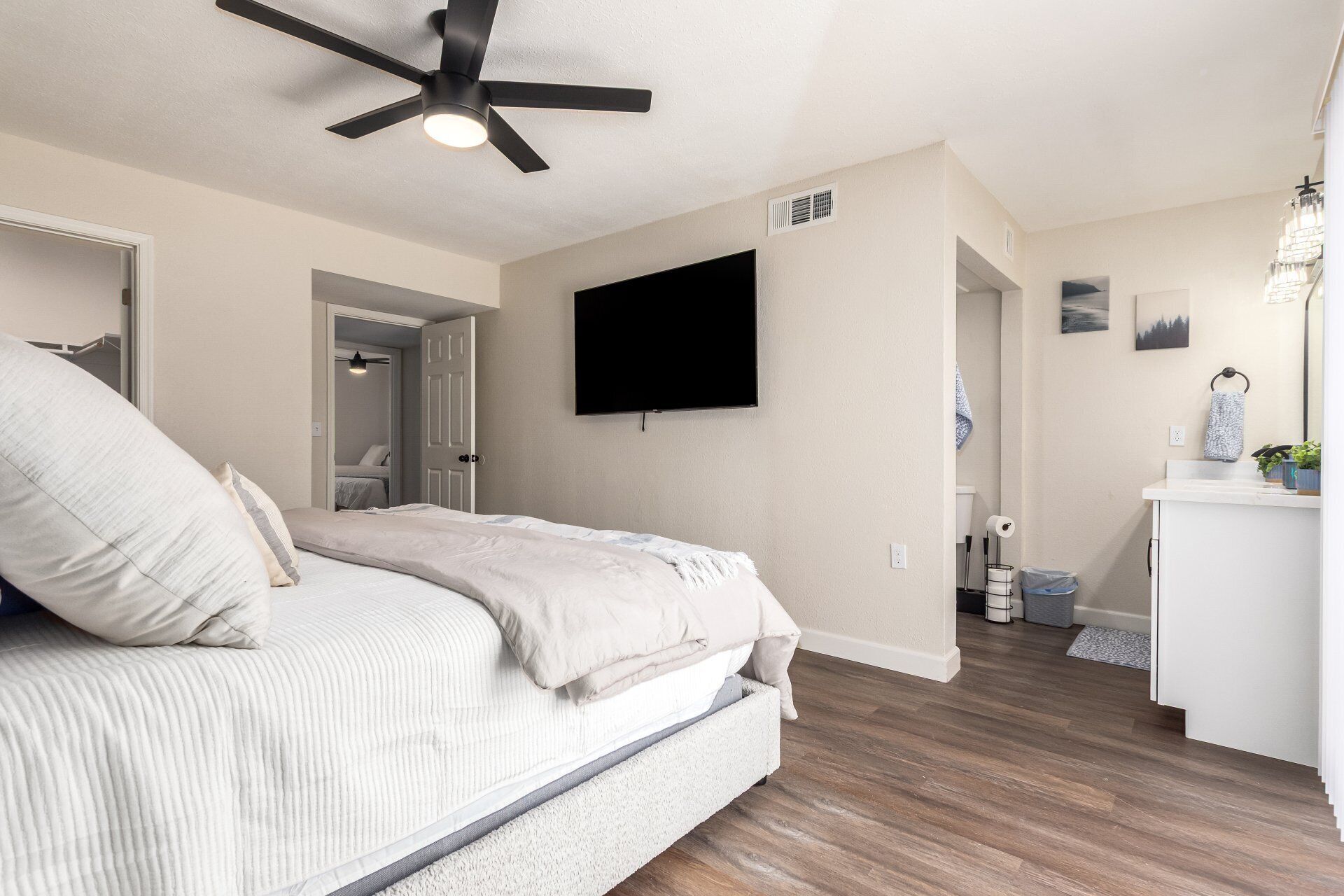 A bedroom with a bed, a ceiling fan, a TV, and a bathroom with a toilet and sink.