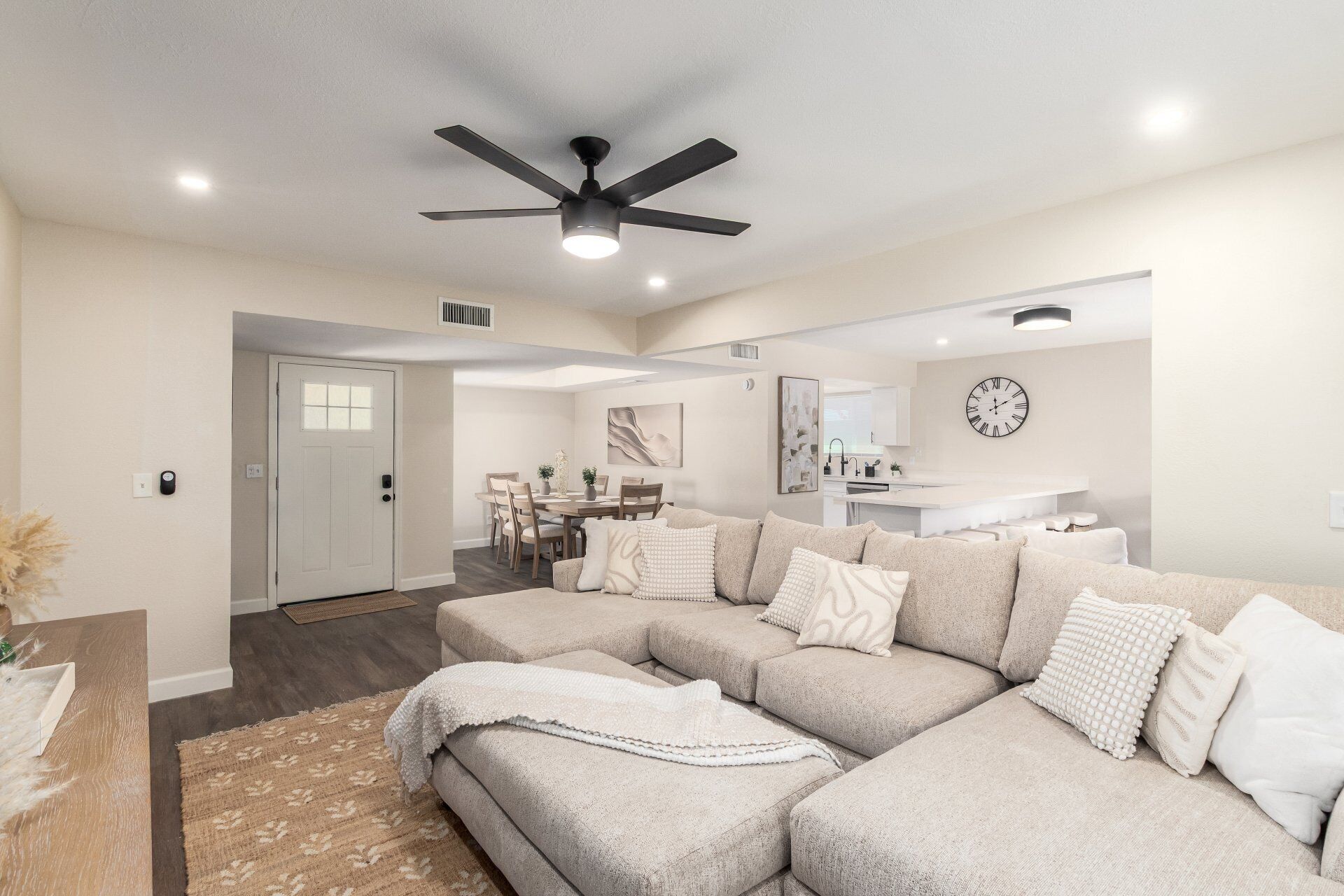 A modern living room with a sectional sofa, a ceiling fan, and a dining area in the background.