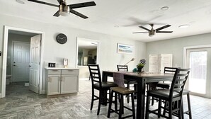Eine geräumige Küche mit Essbereich, zwei Deckenventilatoren, einer Uhr und Blick auf den angrenzenden Wohnbereich.
