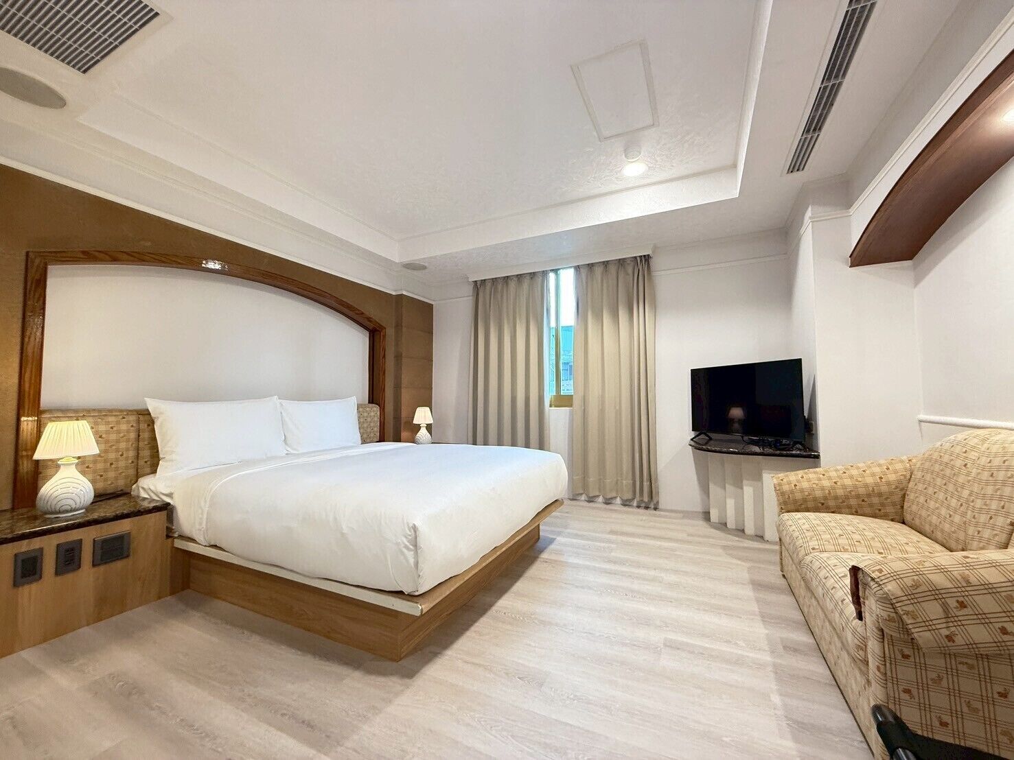 Una habitación de hotel con una cama grande, televisión, sofá y ventana con cortinas.