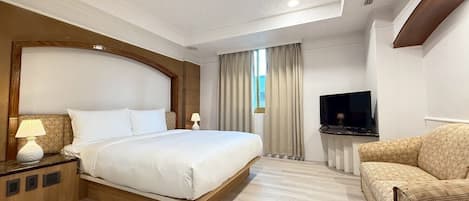 Una habitación de hotel con una cama grande, televisión, sofá y ventana con cortinas.