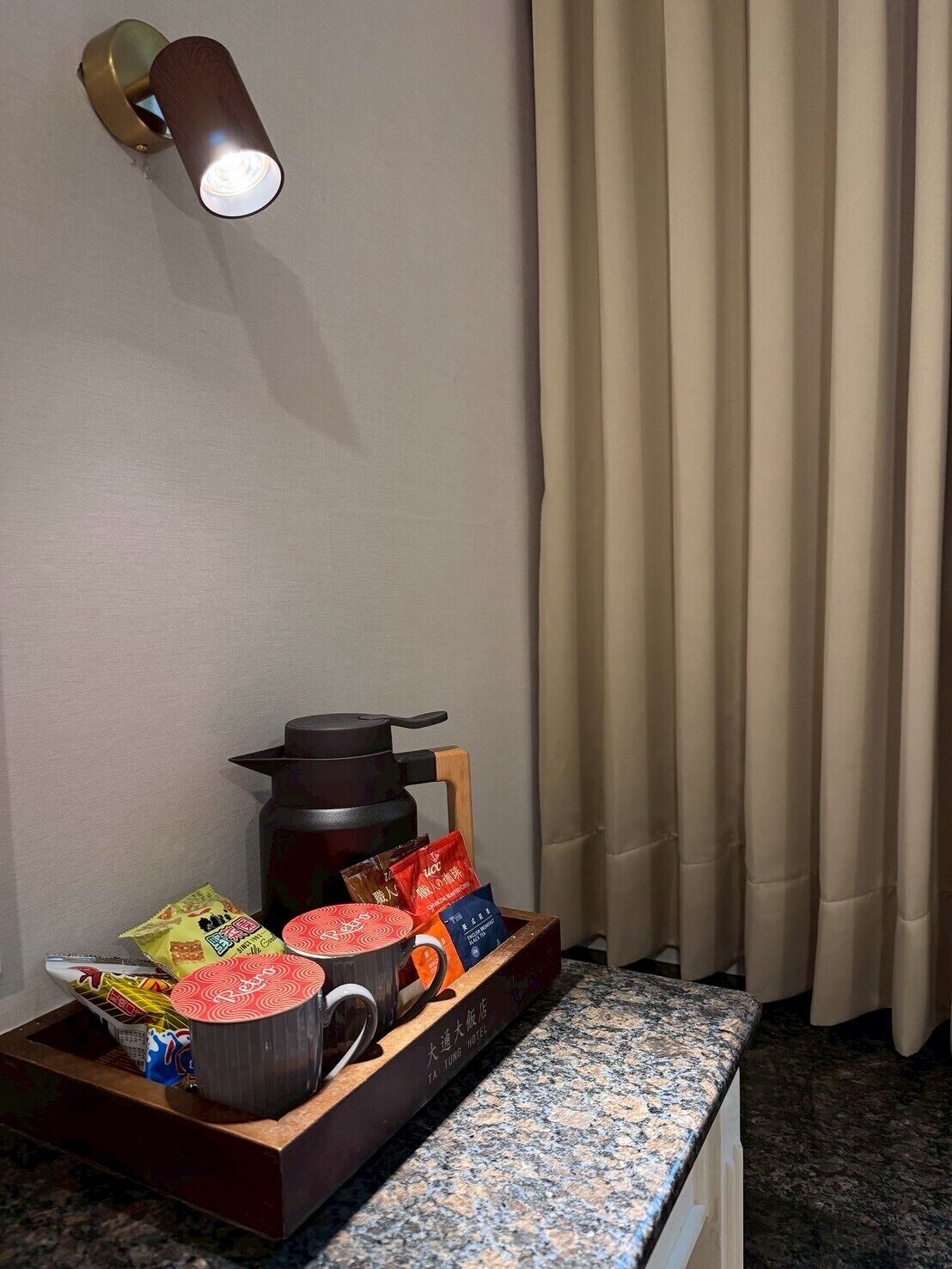 Een hotelkamer met een houten dienblad met snacks, een theepot en een waterkoker.
