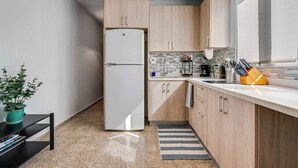 A modern kitchen with light wood cabinets, a white refrigerator, a tiled backsplash, and a countertop with kitchen utensils.