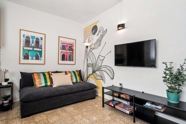 A modern living room with a dark sofa, colorful cushions, a flat-screen TV, a black entertainment unit, and a large plant.
