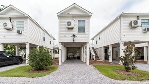 A three-story building with a central entrance, air conditioning units on each floor, and a gravel driveway.