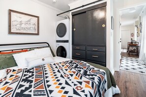 A bedroom with a bed, a large dark wardrobe, a washing machine, and a framed picture on the wall.
