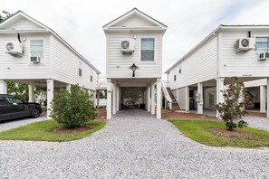 A three-story building with a central entrance, air conditioning units on each floor, and a gravel driveway.