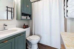 A bathroom with a white sink, green cabinets, a white toilet, and a white shower curtain.