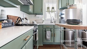 A kitchen with green cabinets, a stainless steel refrigerator, a hanging plant, and a coffee station.