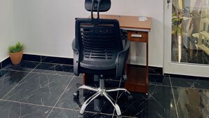 Une chambre d’hôtel avec un fauteuil de bureau noir, un bureau en bois et un climatiseur fixé au mur.