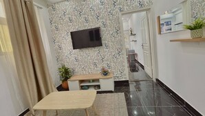 Un salon moderne avec un téléviseur à écran plat fixé au mur, une table en bois, une plante en pot et un papier peint à motifs.
