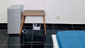 Une chambre à coucher comprenant un lit, une petite table, un réfrigérateur et deux étagères murales décoratives.