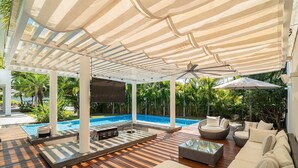 Un espace extérieur abrité comprenant une piscine, des chaises longues et un ventilateur de plafond.