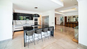 Une cuisine moderne dotée d’un plan de travail en marbre, d’appareils électroménagers noirs et d’un coin repas en verre avec des tabourets de bar.
