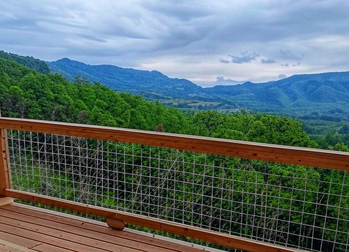 Une terrasse en bois avec une rambarde en métal, d’où l’on peut admirer un paysage montagneux.
