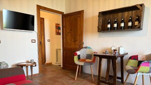 A living room with a sofa, a table with chairs, a TV, and a wine rack. - Cosy apartment for 4 people with WIFI, A/C and panoramic view (Cortona)