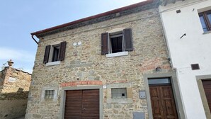 A stone building with two wooden doors and windows, a brick archway, and a small window with a shutter. - Lovely apartment for 4 people with WIFI, A/C and panoramic view (Cortona)