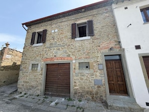 A stone building with two wooden doors and windows, a brick archway, and a small window with a shutter.
