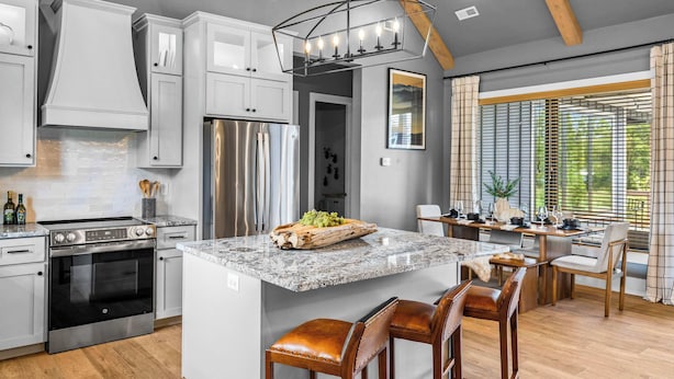 A modern kitchen with white cabinets, a stainless steel refrigerator, and a granite island with bar stools.