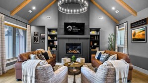 A modern living room with a fireplace, leather sofas, and a chandelier.
