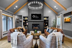A modern living room with a fireplace, leather sofas, and a chandelier. - Luxury Cabin, Sleeps 12・Pool, Hot Tub + Family Fun (Sevierville)