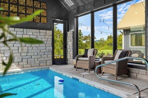A pool area with a clear view of the outdoors, a stone wall, and wicker furniture.