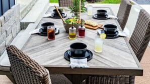 An outdoor dining area with a table set for two, surrounded by wicker chairs.
