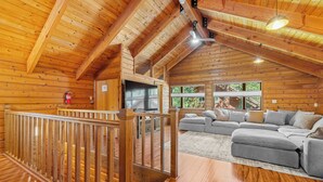 A spacious living area with a large gray sectional sofa, wooden flooring, and a wooden ceiling with exposed beams.