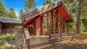 A wooden cabin with a porch, surrounded by trees.
