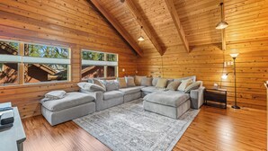A cozy, wooden-paneled room with a large L-shaped sectional sofa, a rug, and a desk with a lamp.
